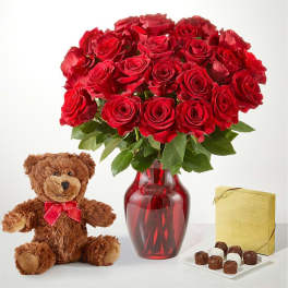 Red roses in a glass vase with a teddy bear and chocolates