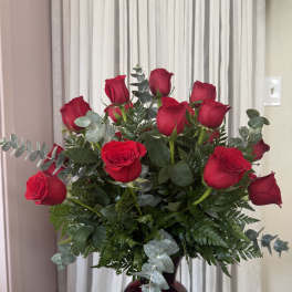 Red roses arranged in a dark glass vase with eucalyptus