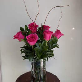 Pink roses arranged in a clear glass vase with tall curly branches