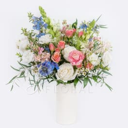 Mixed bouquet of pink, white, and blue flowers in a white vase