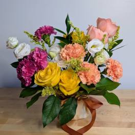 Bouquet of yellow roses, pink carnations, and white lisianthus in a wrapped vase