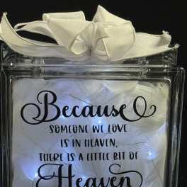 Lighted glass block with white feathers, ribbon, and a memorial quote about a loved one in heaven.