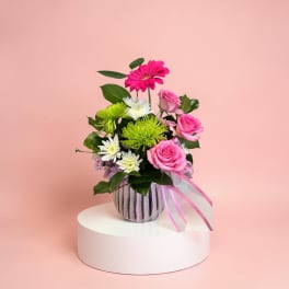 Pink and white flowers in a striped vase with a ribbon