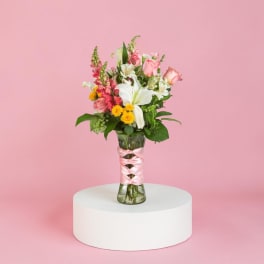 Pink and white mixed bouquet in a glass vase with a pink ribbon