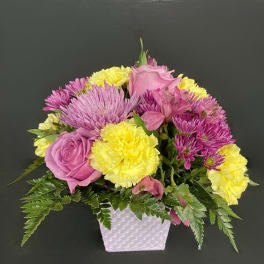 Pink and yellow flower arrangement in a white square vase