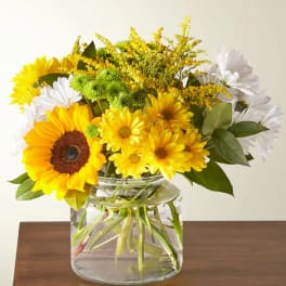 Yellow sunflowers and white daisies in a clear glass vase