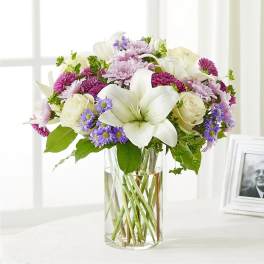 Bouquet of white lilies, roses, and purple daisies in a glass vase