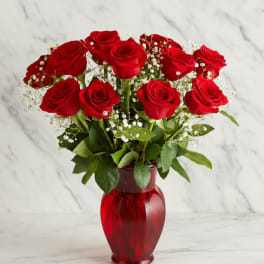 Red roses arranged in a red glass vase with baby's breath