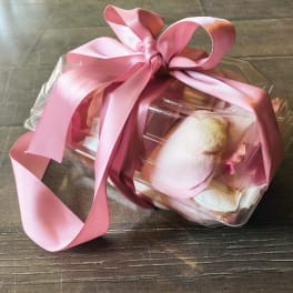 Clear gift box tied with a pink ribbon, holding pale pink and white items