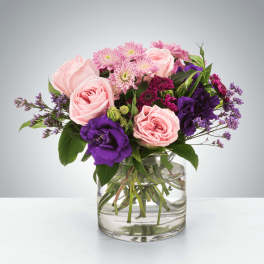Pink roses and purple flowers arranged in a clear glass vase