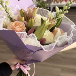 Hand-tied bouquet of white and peach roses with pink lilies, wrapped in lavender paper with ruffled white trim