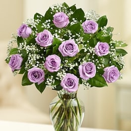 Vase of light purple roses with white filler flowers in a clear glass vase