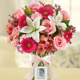 Pink and white mixed bouquet in a clear glass vase with a pink bow and small photo frame charm