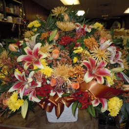 Large mixed floral arrangement with lilies, roses, and chrysanthemums in a white container