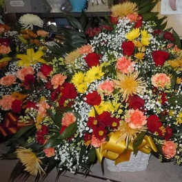 Large mixed flower arrangement with red roses, yellow blooms, and peach carnations