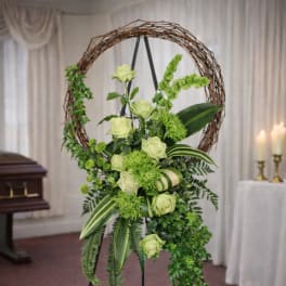 Green floral wreath on a stand with pale roses and trailing greenery
