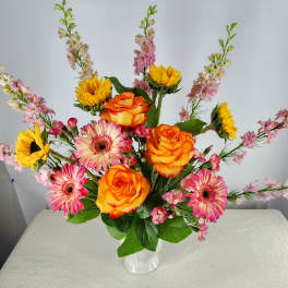 Mixed bouquet of orange roses, pink gerberas, and yellow sunflowers in a white vase