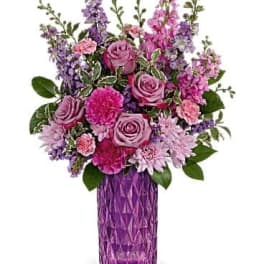 Tall arrangement of pink and purple roses, carnations, and mums in a faceted purple glass vase