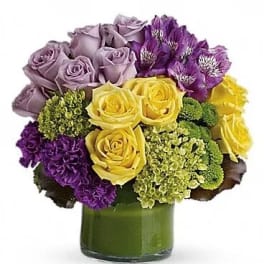 Bouquet of yellow, lavender, and purple flowers in a green glass vase