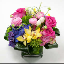 Colorful bouquet with pink roses, yellow orchids, and blue hydrangeas in a glass vase