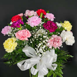 Bouquet of multicolored carnations in a glass vase with a white ribbon