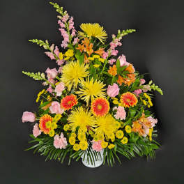 Tall fan-shaped arrangement of yellow and orange blooms with pink accents in a white container