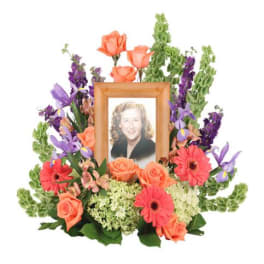 Framed portrait surrounded by orange roses, purple flowers, and pink gerberas