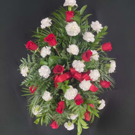 Red roses and white carnations in a standing spray with a red ribbon