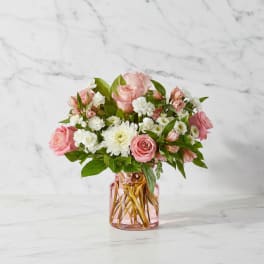 Pink roses and white flowers arranged in a pink glass vase