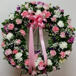 Heart-shaped floral wreath with pink ribbon on a stand