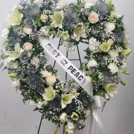 Heart-shaped funeral wreath with white and pale green flowers and a peace ribbon