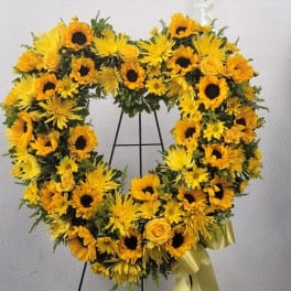 Heart-shaped yellow floral wreath on a stand with a ribbon