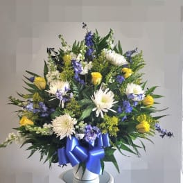 Large bouquet of white and yellow flowers with a blue ribbon in a white vase