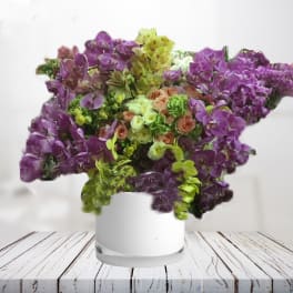 Purple and green orchid arrangement in a white vase