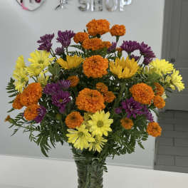 Bouquet of orange marigolds and yellow and purple daisies in a glass vase