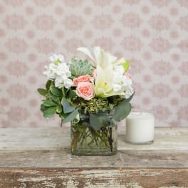 Pink roses and white lilies arranged in a glass vase beside a white candle.