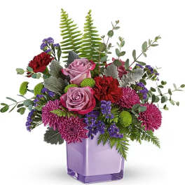 Mixed bouquet of pink roses, purple mums, and red carnations in a lavender vase