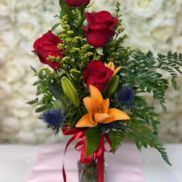 Red roses and orange lilies in a glass vase with ribbon