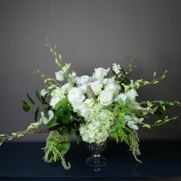 White floral arrangement in a glass vase with trailing greenery