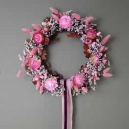 Pink floral wreath with ribbon tails on a gray wall