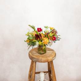 Mixed bouquet in a glass jar on a wooden stool