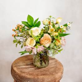 Cream and peach roses in a glass vase with small white flowers