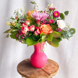 Mixed bouquet of pink, peach, and white flowers in a bright pink vase