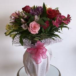 Mixed bouquet of roses and alstroemeria in a wrapped vase with a pink ribbon