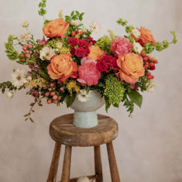 Mixed bouquet of peach, pink, and white flowers in a pale vase