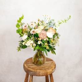 Mixed pastel bouquet in a glass vase on a wooden stool