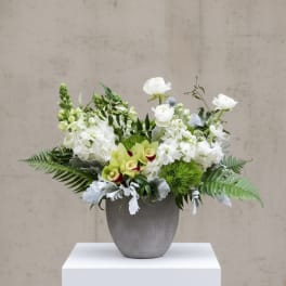 Low white and green floral arrangement with orchids and round white blooms in a gray pot.