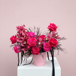 Pink roses and orchids in a pink hat box with black ribbon