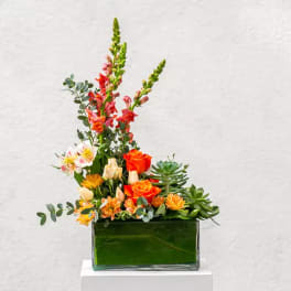 Mixed floral arrangement in a green glass vase with orange roses and pink snapdragons
