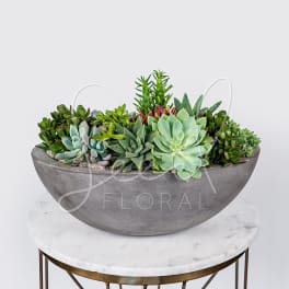 Succulent arrangement in a gray bowl planter on a round table